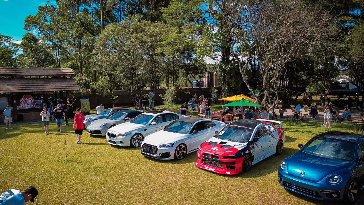 Fila de carros expostos sob as árvores, com visitantes ao fundo