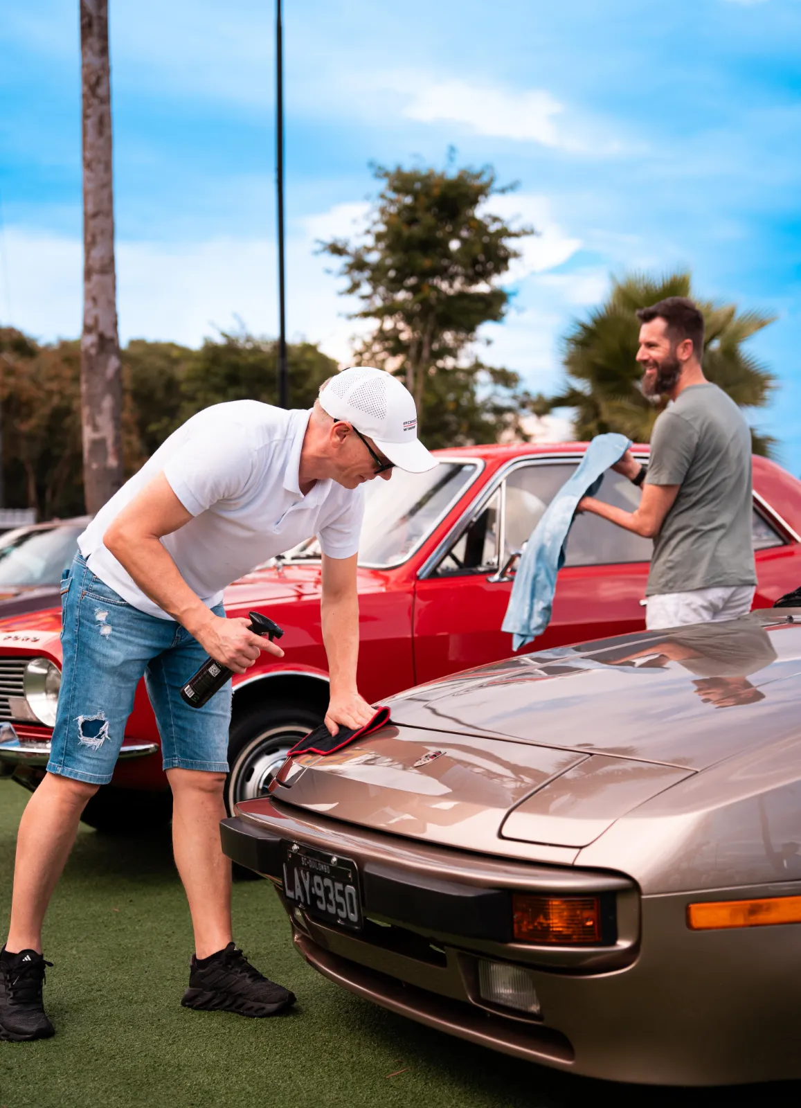 Participantes polindo um Porsche 944 e uma Alfa Romeo vermelha no gramado do evento